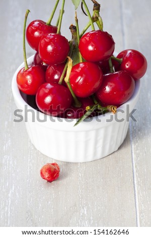 Freshly picked cherries with stem and leaves in a white bowl, in front is a cherry pit