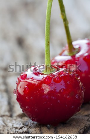 Extreme closeup of a fresh cherry with stem and big sparkling water drops on a old wooden Table