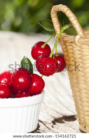 Cherries with sparkling Water Drops are hanging on the side of a basket, other Cherries are in a white Bowl on a old Wooden Table