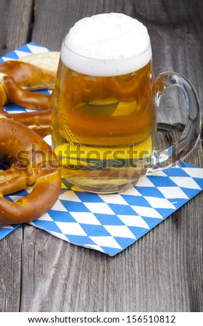 A cold beer in a beer glass with engraving and pretzels on napkins with blue and white rhombuses on a rustic wooden table