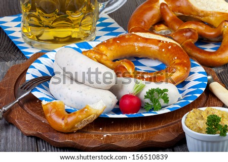 Typical Bavarian Oktoberfest snack with white sausage, mustard on a paper plate, a glass of beer and pretzels on an old rustic wooden table