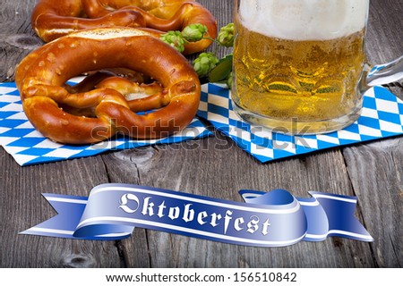 A beer mug and pretzels on napkins with blue and white rhombuses on a rustic wooden table at the bottom a blue banner with the words Oktoberfest