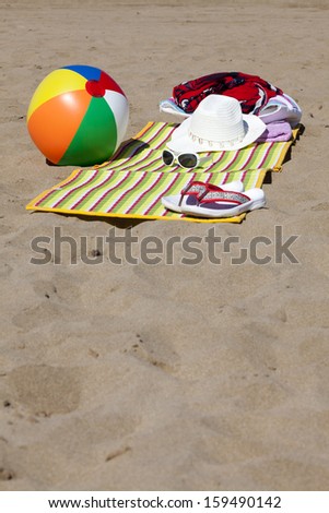 Beach scene in the Summer with Flip-Flops, Beach Ball, Towel, Sunglasses and Straw Hat with Copy Space in lower part of image