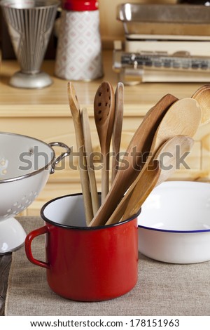 Cooking utensils are on a table in the background is a kitchen cupboard with measuring cup and kitchen scale