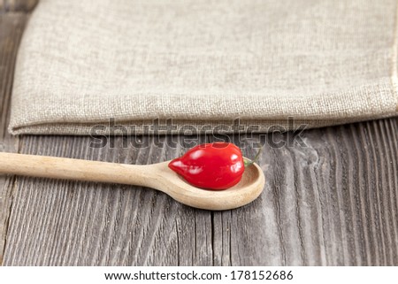 Red Habanero chili pepper on a wooden spoon on a rustic wooden board with copy space in the upper area of the image