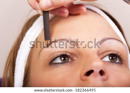 Beautician applying eyebrow pencil for darkening the Eyebrows of a young Woman