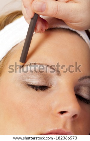 Beautician applying eyebrow pencil for darkening the Eyebrows of a young Woman