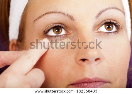 Beautician apply eye shadow with her finger under the eyes of a pretty young woman