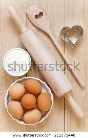 Baking utensils made Ã?Â¢??Ã?Â¢??of wood and eggs and flour in bowls on a wooden table