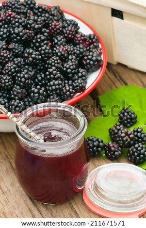 Freshly harvested forest blackberries in a bowl with a glass of blackberry jam on a rustic wooden table in the garden