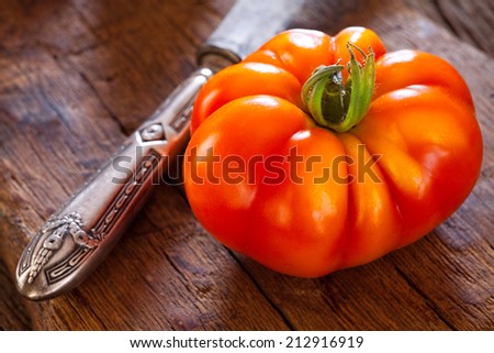 Close up of a ripe beefsteak tomato from their own garden and a table knife on a rustic cutting board in a country style