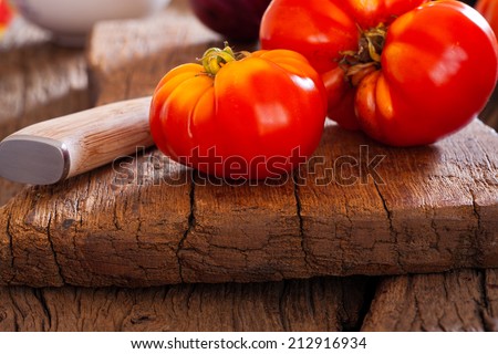 Close up of a ripe beefsteak tomato from their own garden and a kitchen knife on a rustic cutting board in a country style
