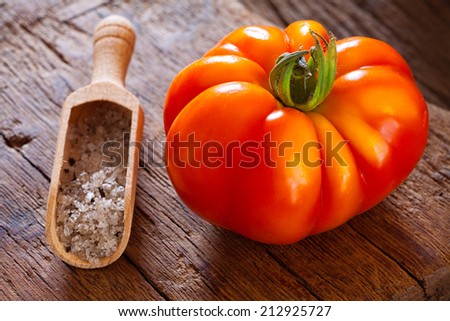 Ripe beefsteak tomato and salt in spice scoop on a rustic wooden board in country style