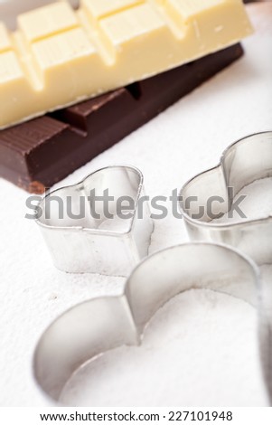 Cookie cutters and white and dark couverture chocolate on floured baking mat