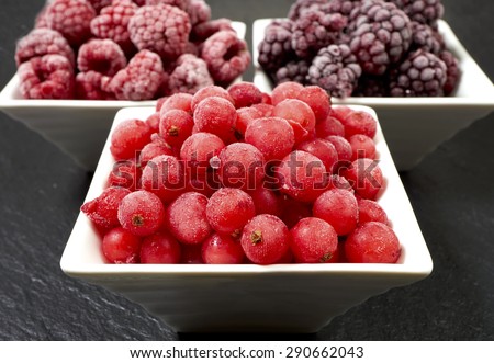 Close-up view of three small porcelain dishes with frozen raspberries, currants and blackberries on a slate platter