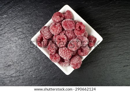 Close up of some frozen raspberries in a white porcelain dish on a slate platter