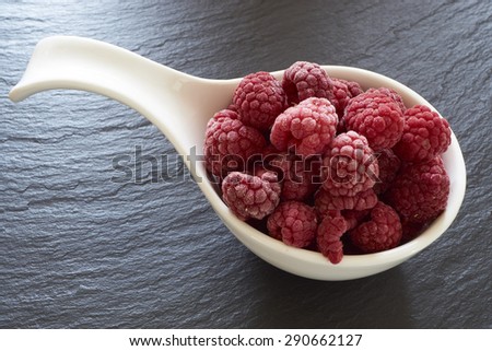 Close up of some frozen raspberries in a white porcelain dish on a slate platter