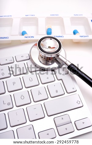 Black Stethoscope lies on computer keyboard and a pill box with labeling time of day in the background