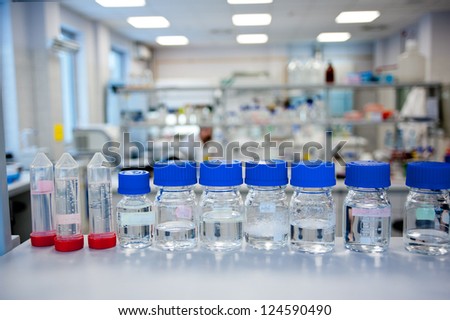 Chemicals reagents in a row in glass bottles placed at laboratory shelf. In background blurred chemical laboratory.