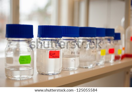 Chemicals reagents in a row in glass bottles placed at laboratory shelf.
