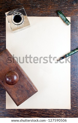 top view of old yellowed sheet of paper at wooden vintage desk. fountain pen, inkstand with black ink and blotting paper.