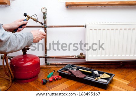 Plumber using welding gas torch to solder copper central heating pipes.