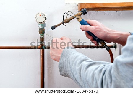 Plumber using welding gas torch to solder copper central heating pipes.