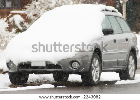 A car sits beside the curb in a residential neighborhood with a coat of fresh snow on its hood.