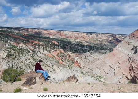 senior man sitting on a rock overlooking desert canyon near Grand Junction, Colorado with the cliffs of the Colorado National Monument in the background and Bangs Canyon in the foreground.