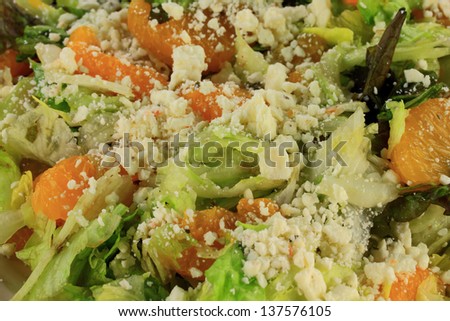 Closeup view of Fresh mixed salad prepared from Chopped Fresh Organic Lettuce and Sections of Mandarin Oranges seasoned with Feta cheese served in gray plate over white background.