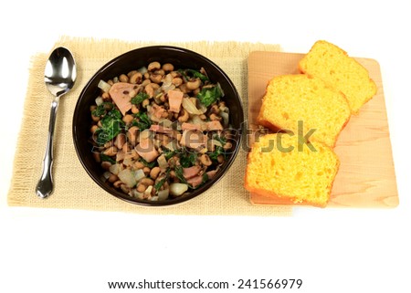 Served in black bowl New Years Day Traditional American South cooked meal, Chopped Ham and Collard Greens, Black-eyed Pea, Onion, white serviette, Slices Corn Bread Spoon over white background