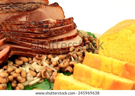 Close-up view of cooked Traditional for American South New Years Day Meal from cooked smoked Spiral-cut of Pork Ham, Black-eyed Peas, over Collard Greens and Corn Bread over white background
