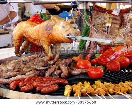 pig, meat and vegetables in course of barbecue preparation at spring fair in barcelona, spain