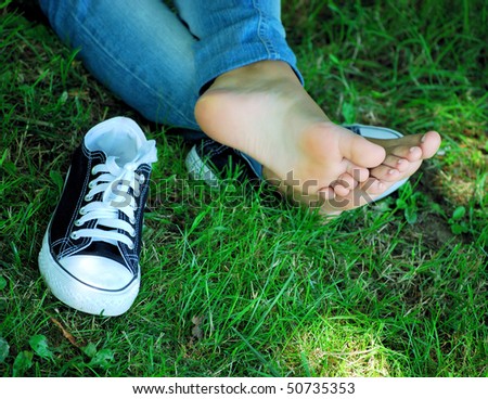 feet of the girl teenager and gym shoes on a green grass of a lawn in park