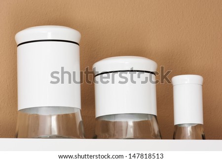 three empty white glass jars on a shelf.