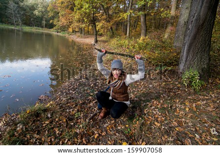 Young beautiful woman makes fun with a wood stick in a forest by autumn.
