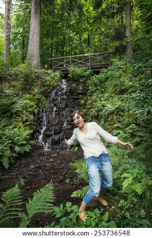 Young woman falls into water. Wooden bridge and waterfall. Hiking theme.