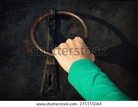 Woman\'s hand knocking on the old door with knocker.