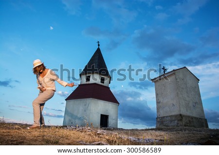 Young caucasian woman imitates guitar playing by the church on the hill.