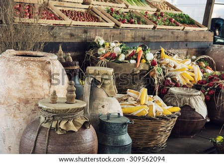 Mix of vegetables in wooden containers and wicker baskets with clay pots and metal milk container in the foreground. Market place.