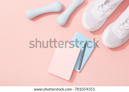 Female sports flat lay, dumbbells, notepad, sneakers on pink background, New Year fitness resolutions