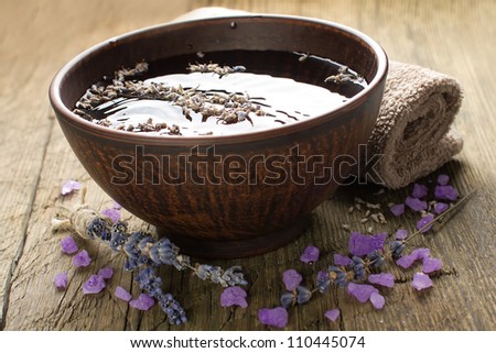 Bowl of pure water and lavender petals on the old wooden surface. Spa treatments composition