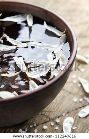 Bowl of water with flower petals and sea salt on a vintage wooden table