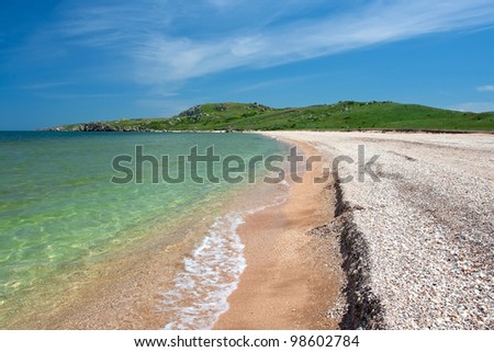 Sunny beach with clear water and green hills in a cozy bay