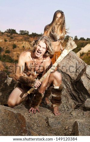 Primitive man holding a club defends his woman. Tribal of a wild people.