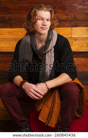 Handsome young man sitting on the suitcase on the wooden background