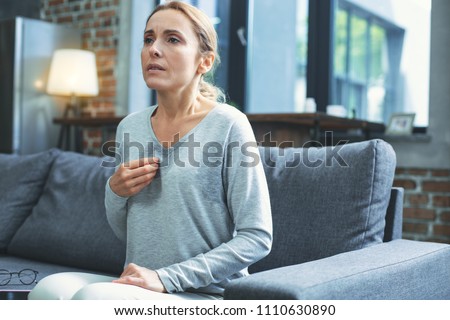 Hot flashes. Exhausted mature woman resting on sofa and having hot flash