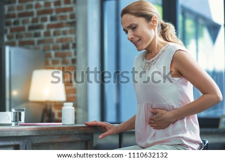 Stomach pain. Worried mature woman touching belly and looking down