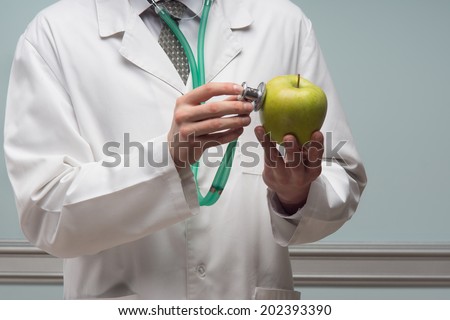 Half- length portrait of the doctor, touching to the green ripe apple with the stethoscope.