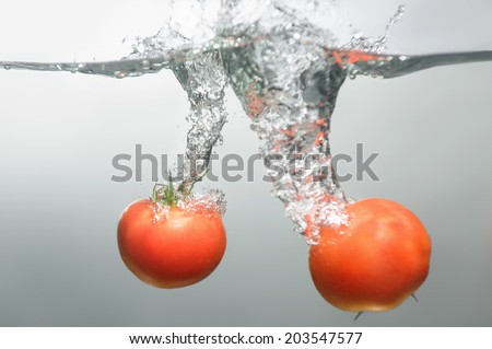 Two red tempting tomatoes dropped into the water spreading little bubbles